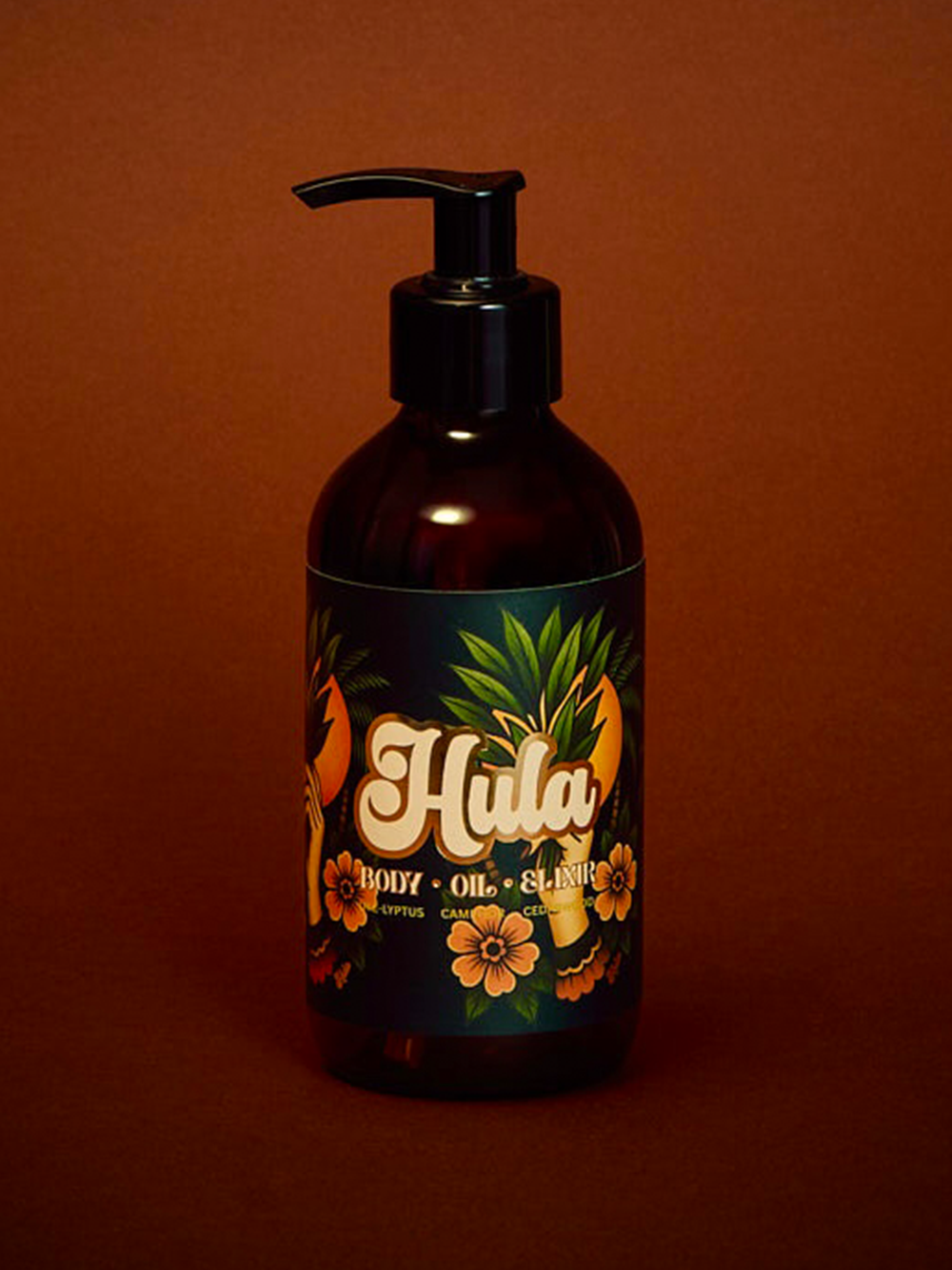 An amber glass pump bottle of Hula Night Camphor Body Oil with a black pump, set against a solid dark reddish-brown background. 