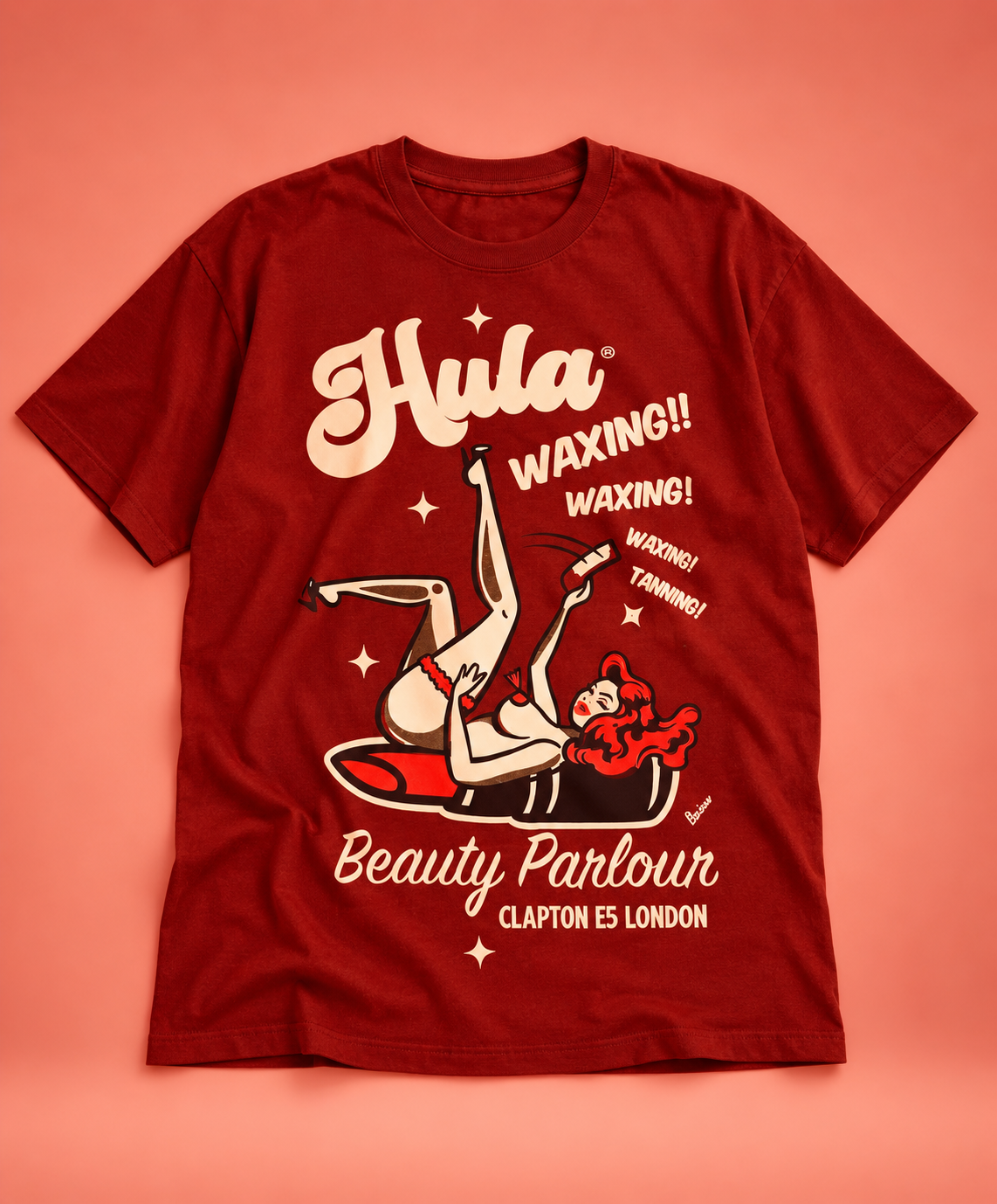 A red mocha short-sleeve T-shirt with a retro pin-up style graphic on the front, featuring the text 'Hula Waxing!!' and 'Beauty Parlour Clapton E5 London' on a solid coral-pink background.