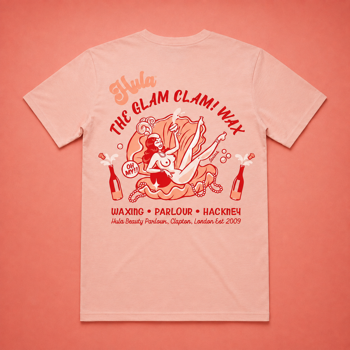A light peach-pink t-shirt shown from the back, featuring a large red and orange graphic print with the text 'Hula THE GLAM CLAM! WAX' and 'WAXING • PARLOUR • HACKNEY'. The background is a solid coral-pink colour.
